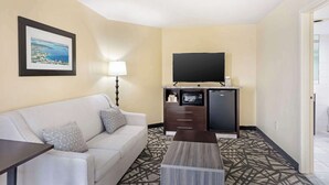 Ein Hotelzimmer mit einer Couch, einem Couchtisch, einem Flachbildfernseher, einer Minikühlschrank und einer Mikrowelle.
