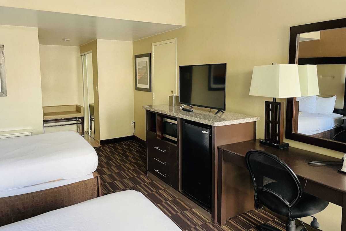 Una habitación de hotel con dos camas, un escritorio con computadora, un televisor y un espejo.