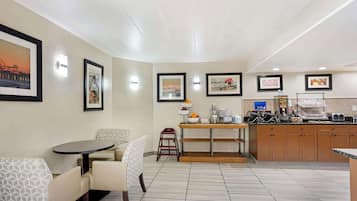 A modern kitchen with a dining area, featuring a round table, chairs, a coffee station, and framed artwork on the walls.