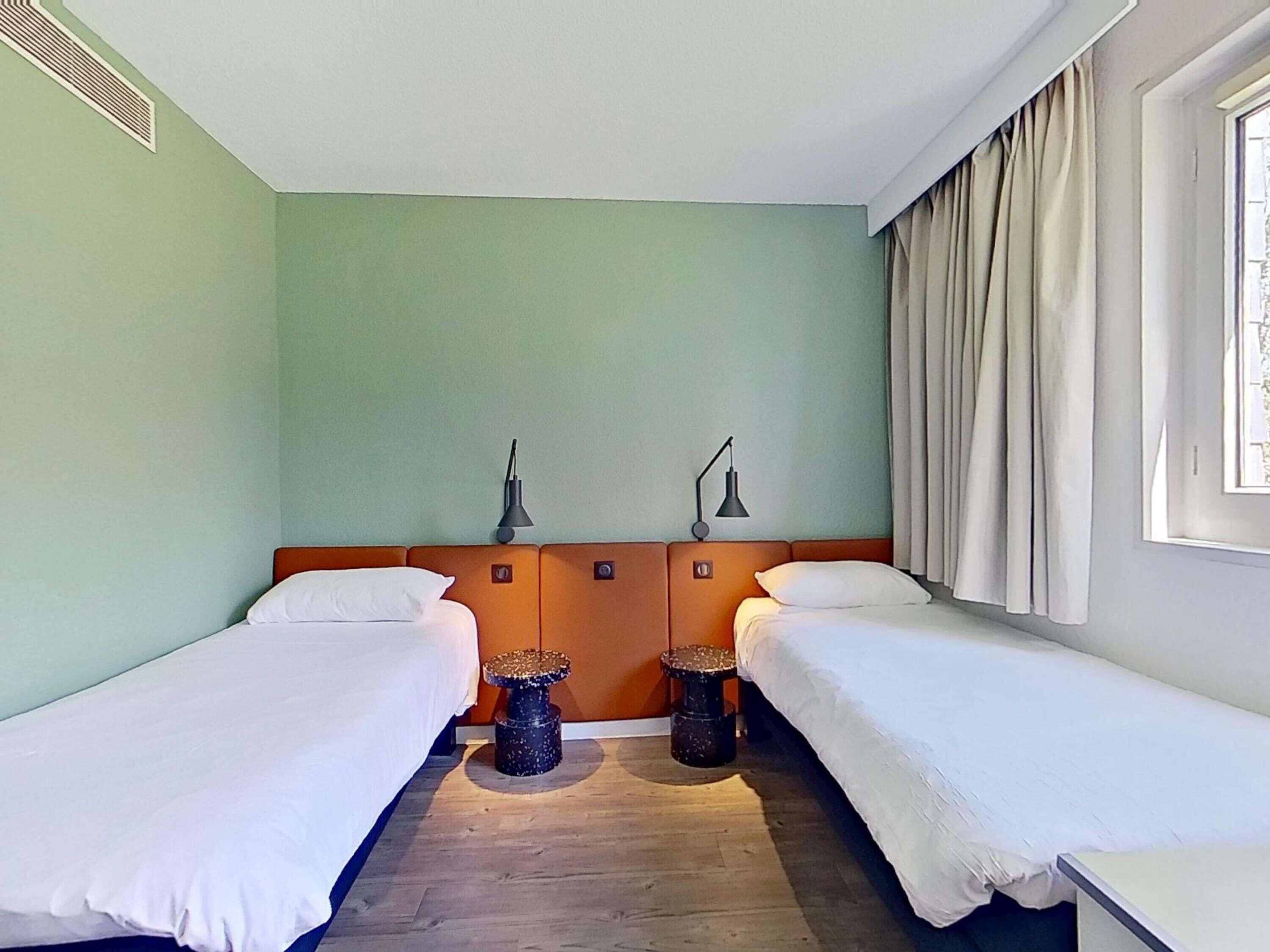Een kamer met twee eenpersoonsbedden, een klein rond tafeltje en een lamp tussen de bedden.