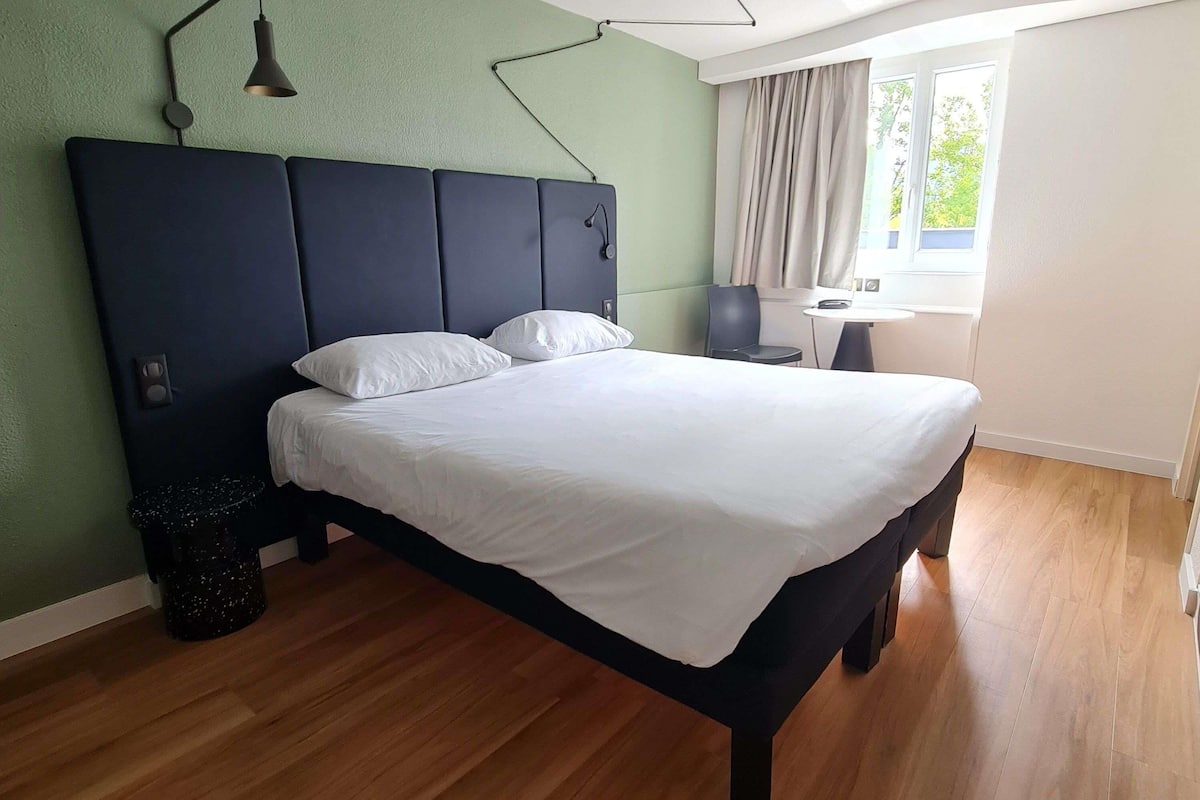 A modern bedroom with a large bed, a desk, and a window with curtains.