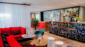 A modern hotel lobby with a red sofa, a bar area with a black and white mural, and a potted plant. - Hotel ibis Vannes (Vannes)