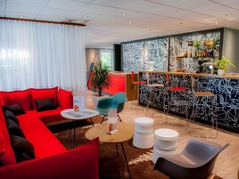 A modern hotel lobby with a red sofa, a bar area with a black and white mural, and a potted plant.
