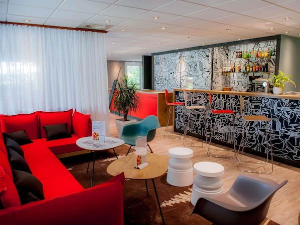 A modern hotel lobby with a red sofa, a bar area with a black and white mural, and a potted plant. - Hotel ibis Vannes (Vannes)