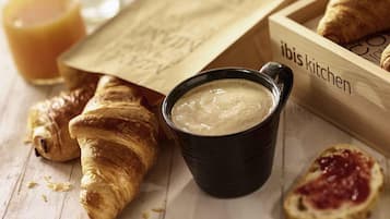 Una bandeja de madera con croissants, una taza negra con una bebida cremosa y pan medio comido con mermelada.
