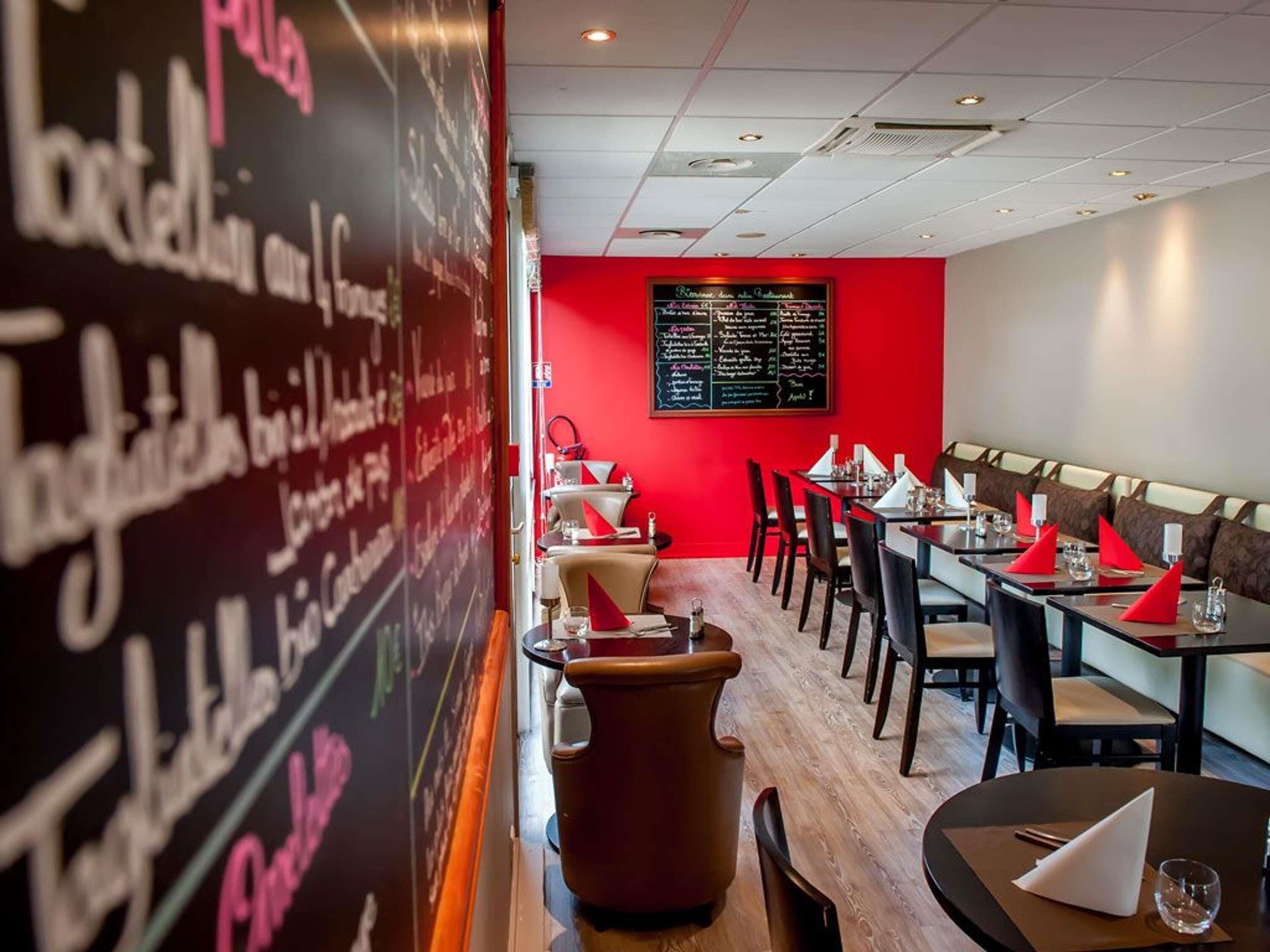 Interior de restaurante con una pared de acento roja, menú en pizarra y varias mesas de comedor.