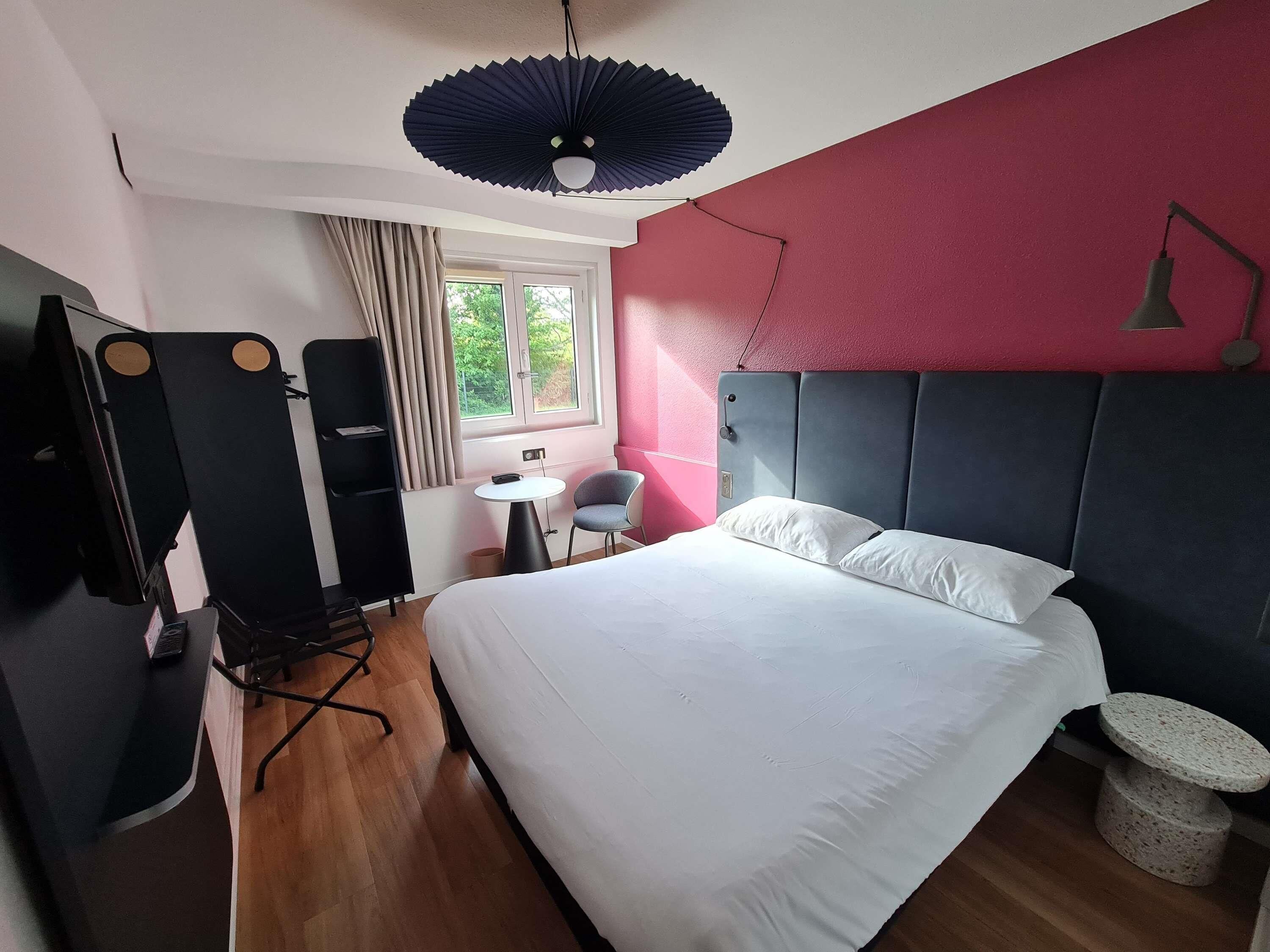Ett hotellrum med en säng, ett skrivbord, en stol, en tv och ett fönster.