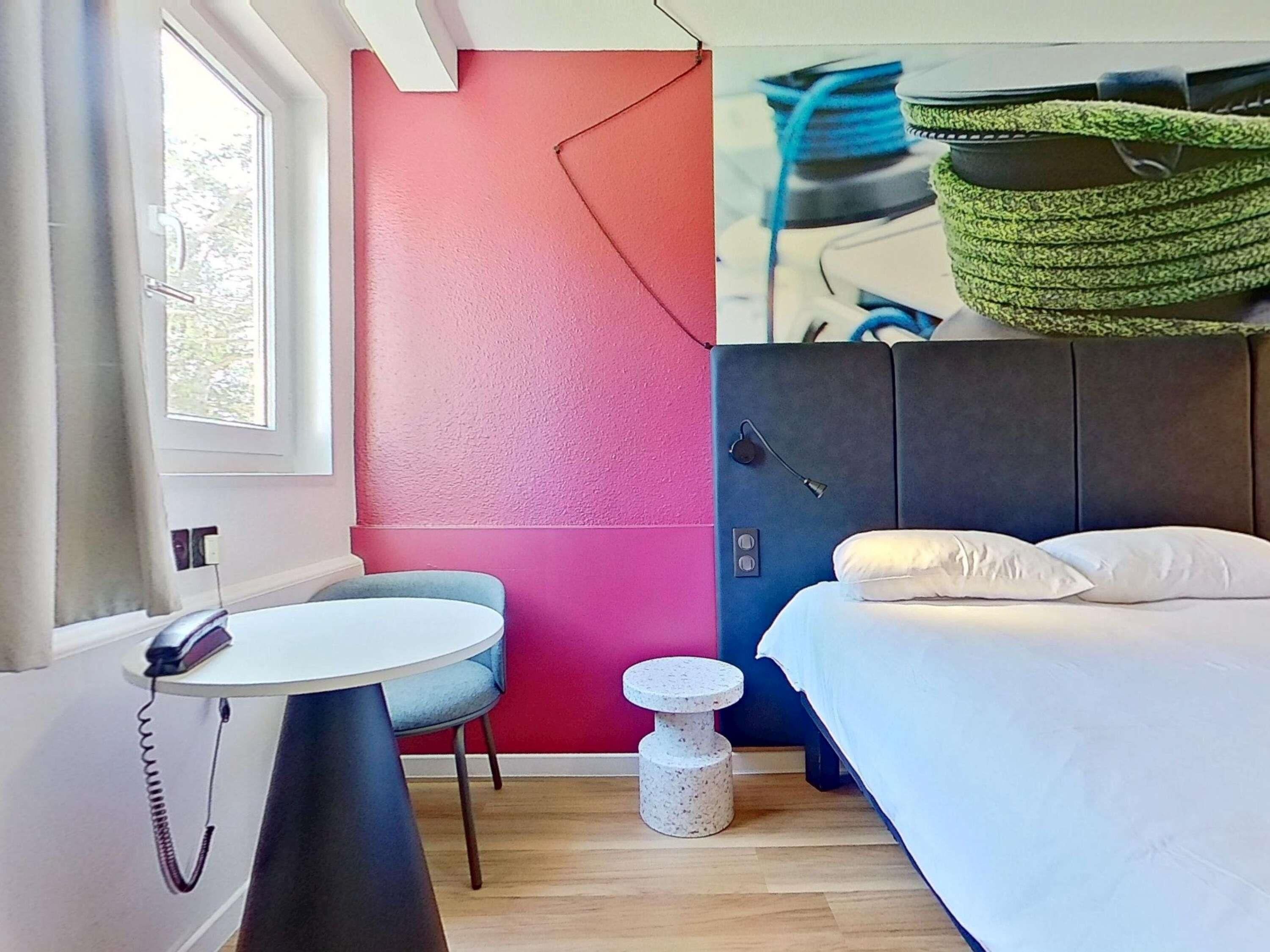 A room with a bed, a desk, a chair, a small round table, and a wall with a colorful design.