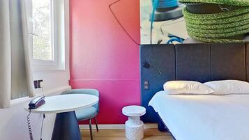 A room with a bed, a desk, a chair, a small round table, and a wall with a colorful design.