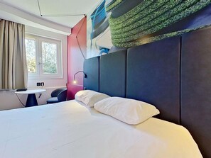 Una camera d'albergo moderna con un letto grande, una scrivania e una finestra con tende.