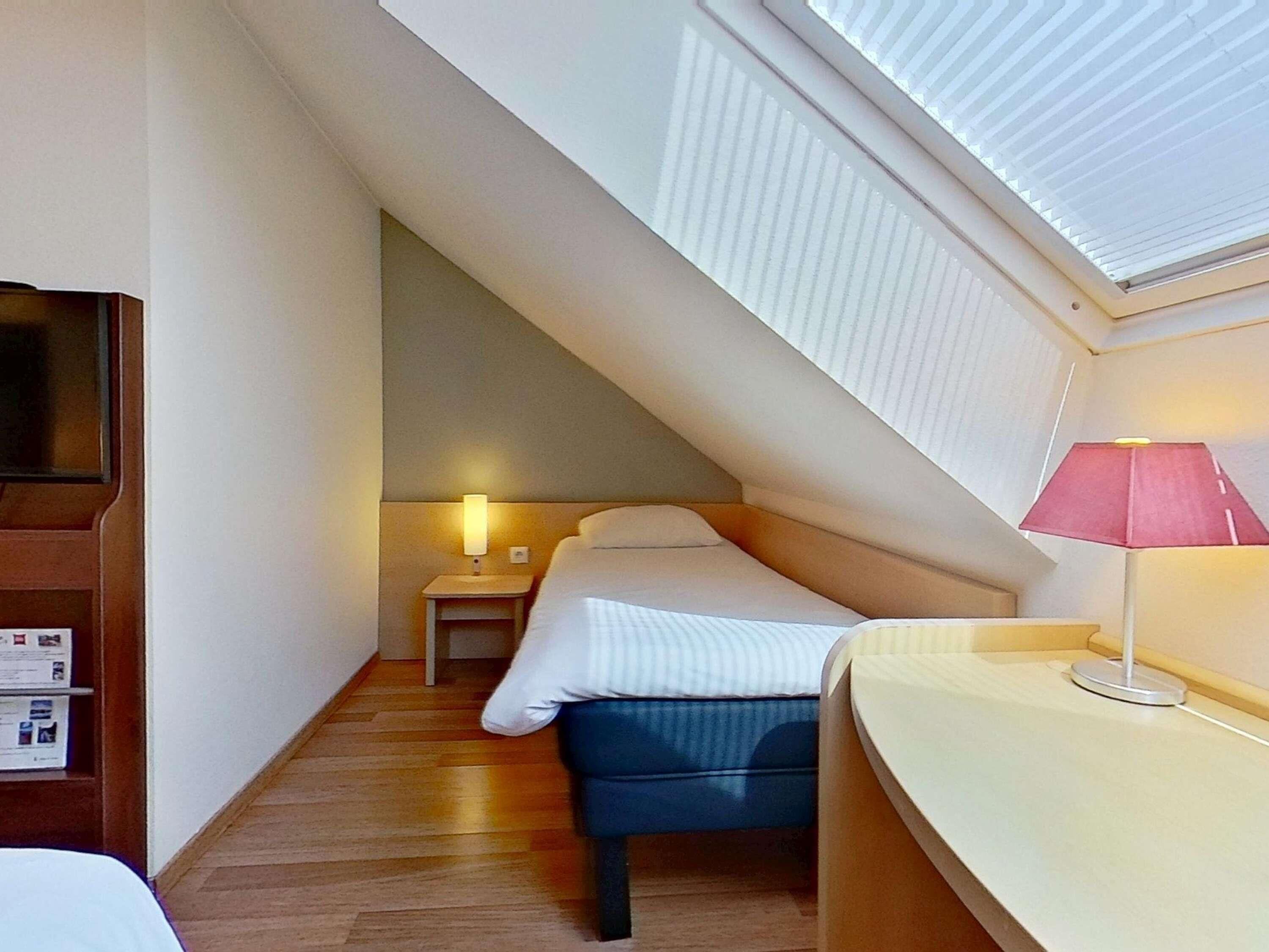 A compact hotel room with a sloped ceiling, a bed, a desk, and a TV.