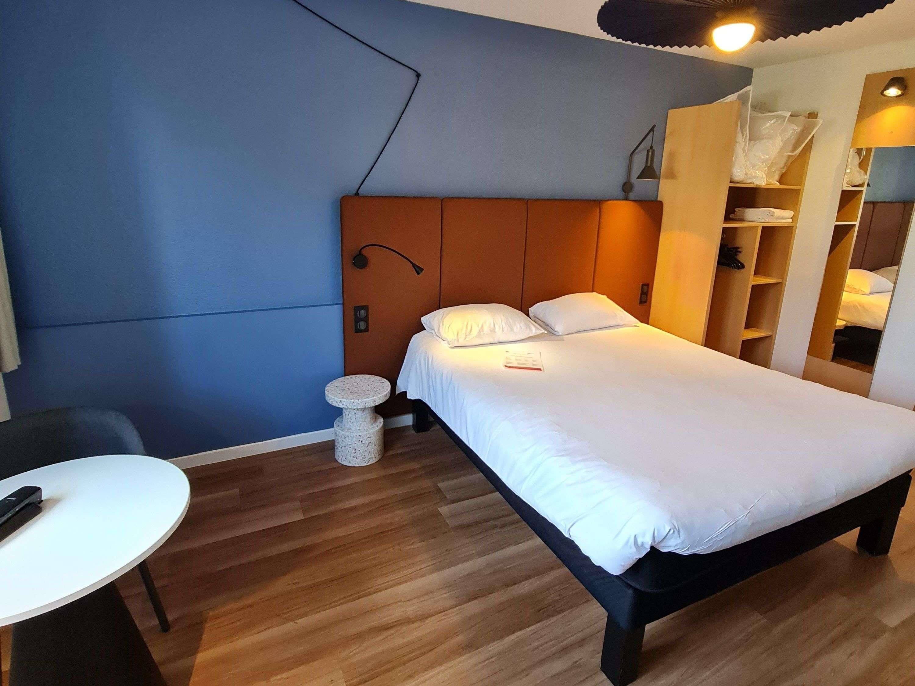 A bedroom with a bed, bedside table, chair, and a small round stool.