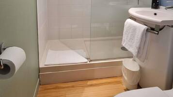 Un baño con inodoro, lavamanos, cabina de ducha de vidrio y un rollo de papel higiénico.