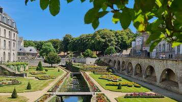 A formal garden with a central water feature, manicured lawns, and a stone bridge.