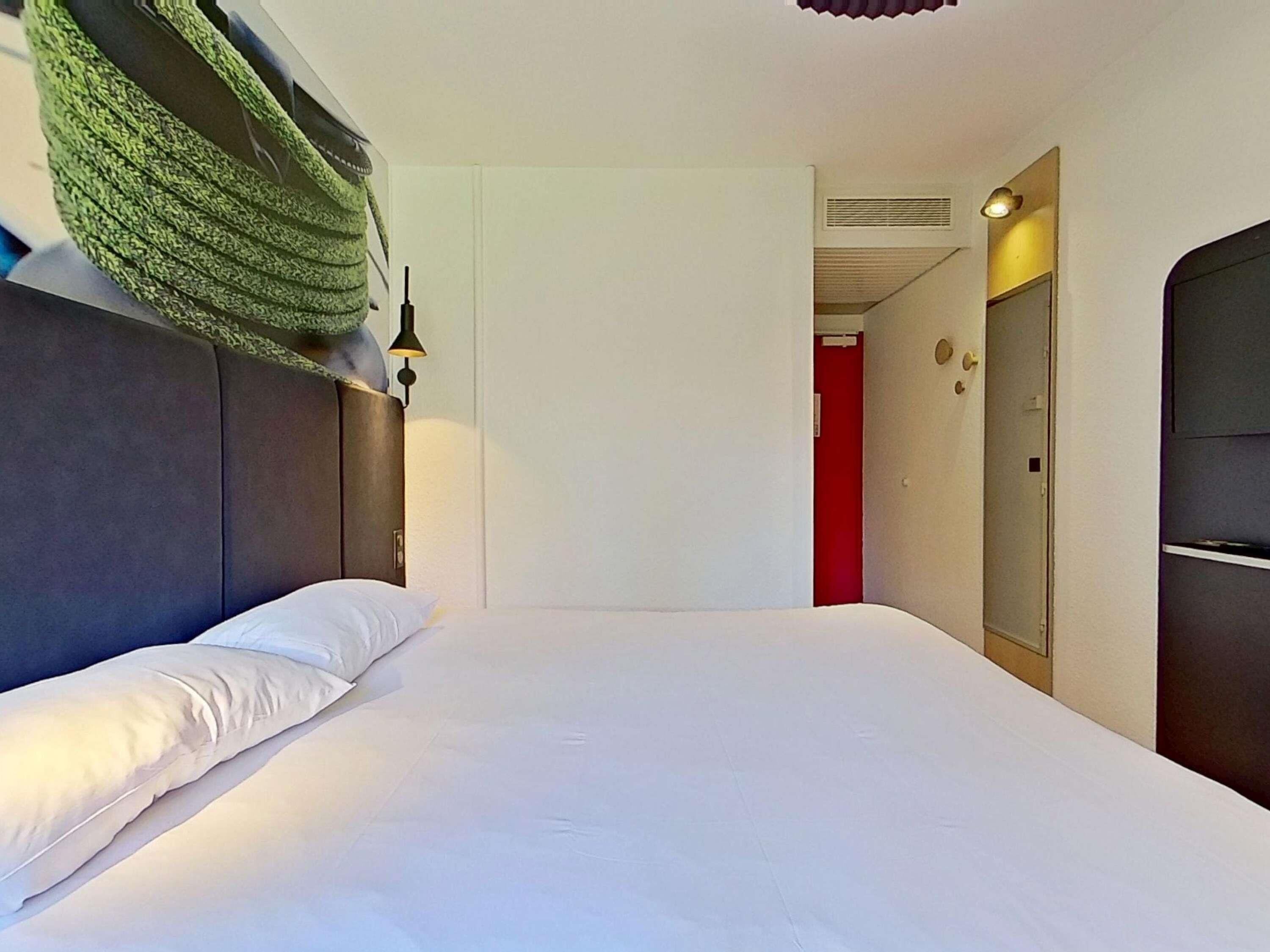 Une chambre d’hôtel avec un lit, un fauteuil suspendu, une armoire et une porte donnant sur une autre pièce.