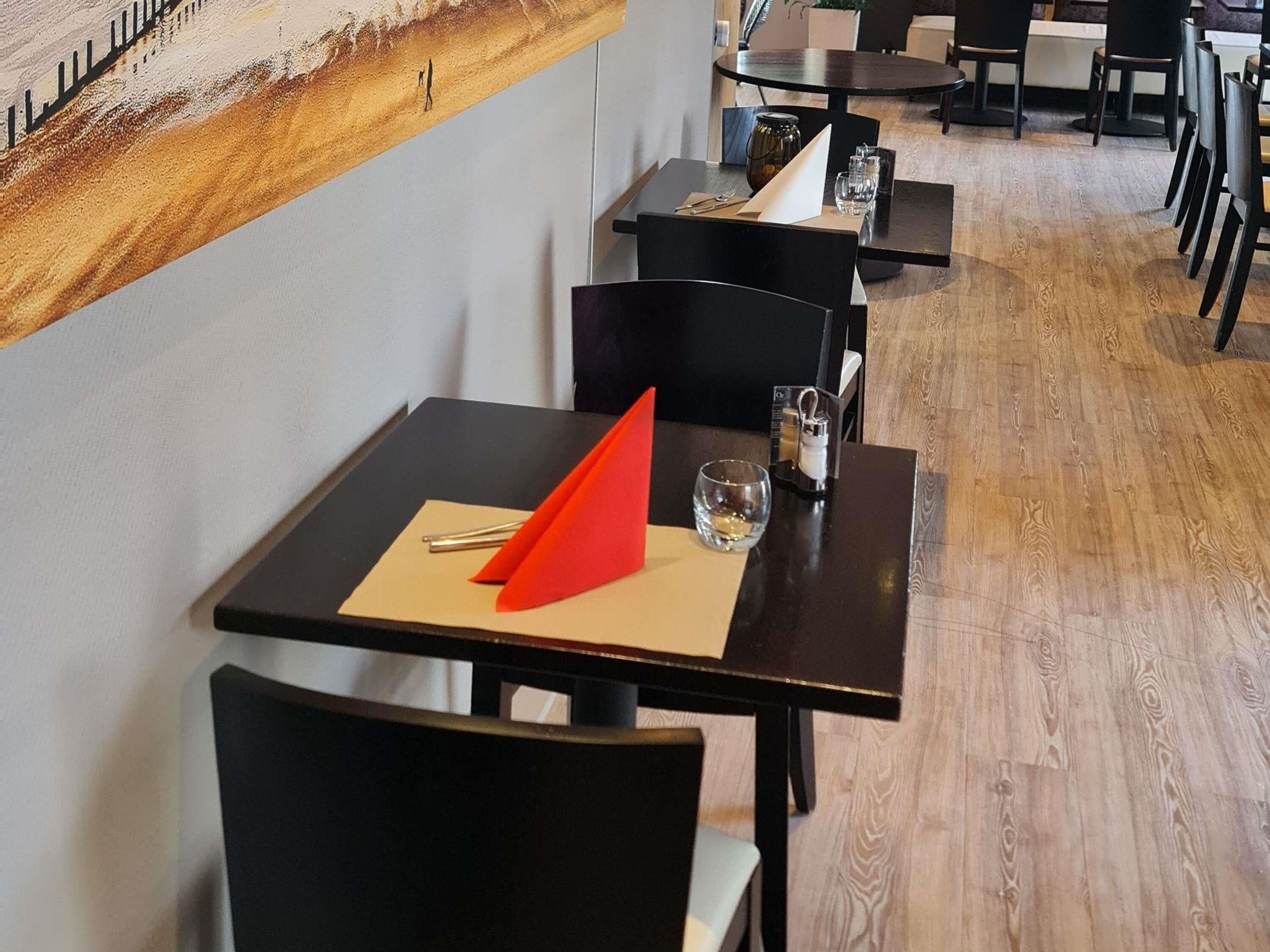 A restaurant with a wooden floor, black chairs, and tables.