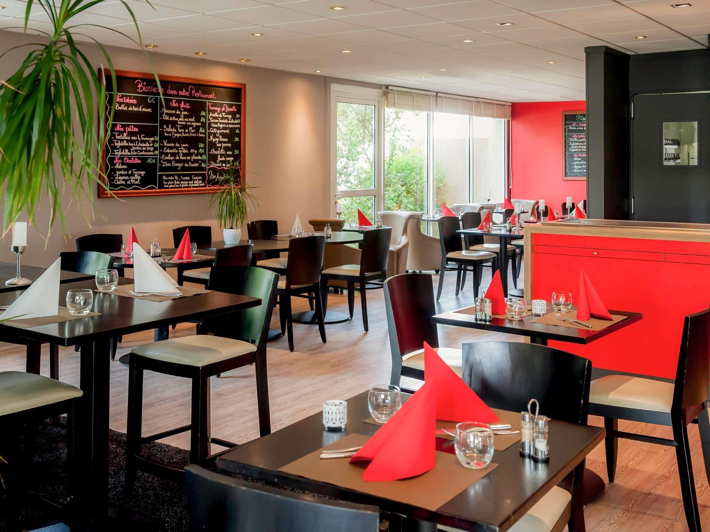 A restaurant with tables set for dining, a chalkboard menu, and a red accent wall.