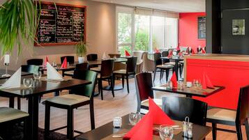 A restaurant with tables set for dining, a chalkboard menu, and a red accent wall.