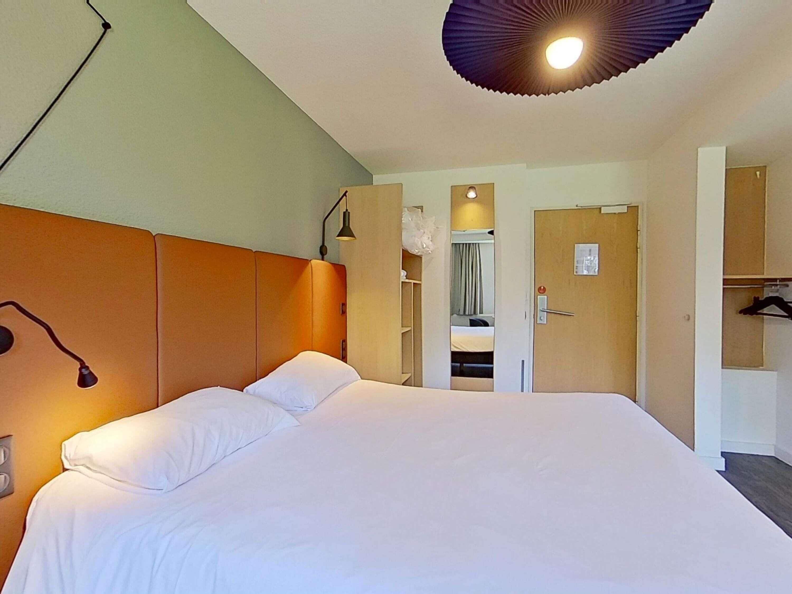 Una habitación de hotel con una cama grande, un armario, un espejo y una lámpara en el techo.