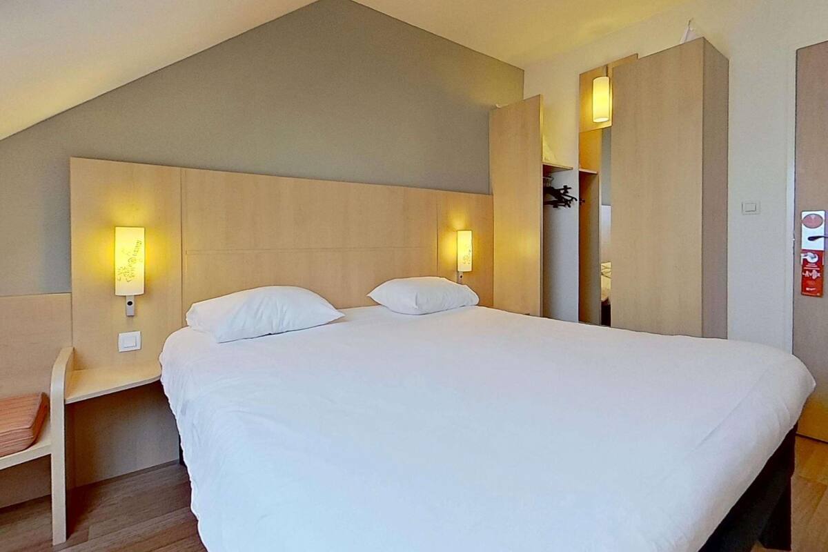 A hotel room with a large bed, two bedside lamps, a desk, and a wardrobe.