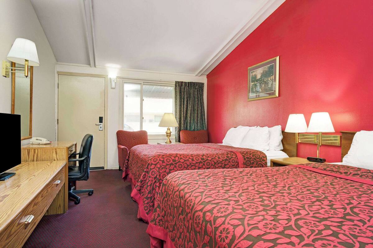 A hotel room with two beds, a desk, a chair, and a TV.