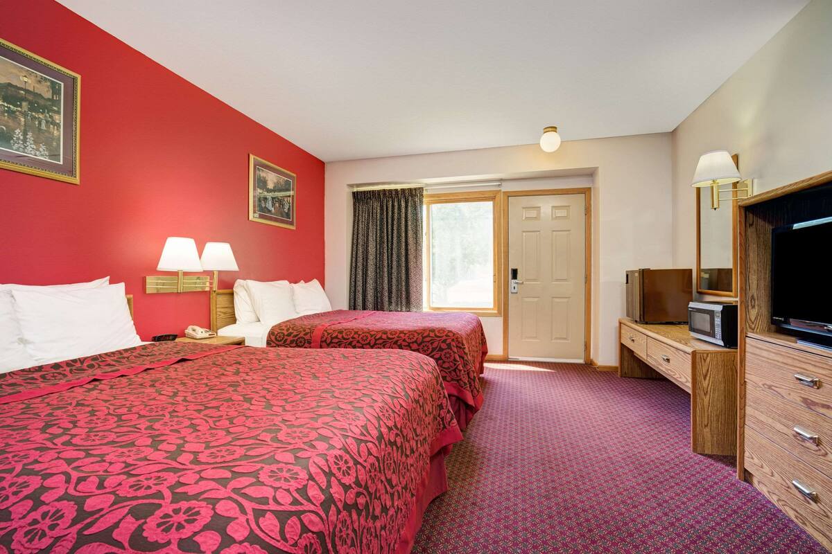 A hotel room with two beds, a desk with a television, a mirror, and a door leading to a balcony.