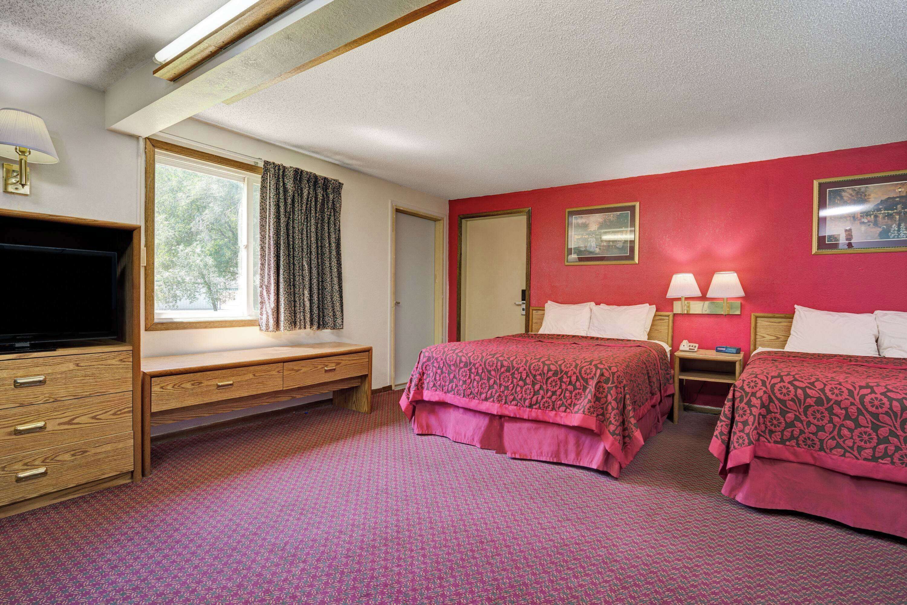 A hotel room with two beds, a TV, a desk, and a window with curtains.