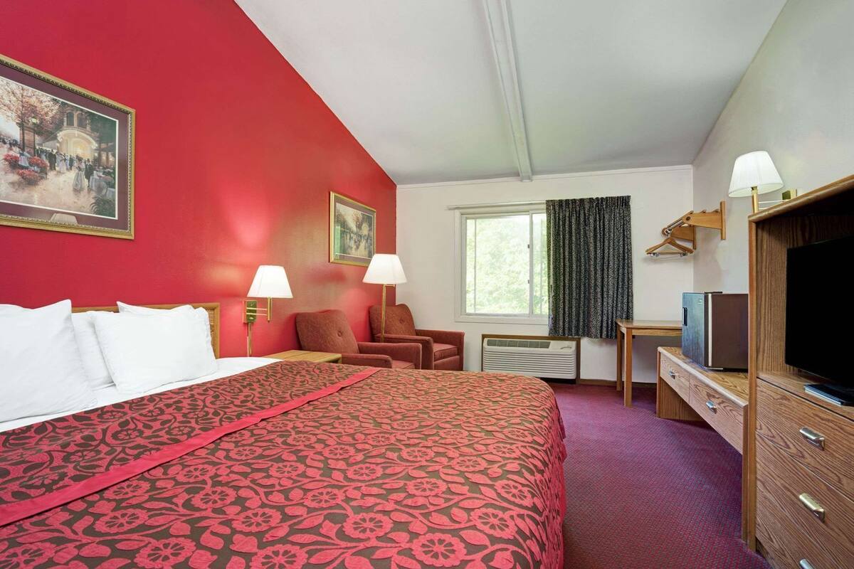 A hotel room with a large bed, two chairs, a desk with a television, and a window with curtains.
