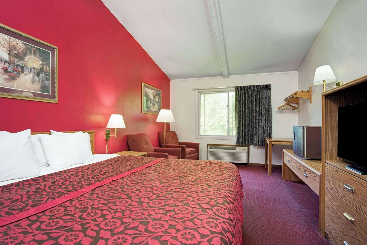 A hotel room with a large bed, a desk with a television, a chair, and a window with curtains.