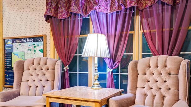 A room with two plush armchairs, a wooden table, a lamp, and a map on the wall. - Travelodge by Wyndham Red Wing (Red Wing)