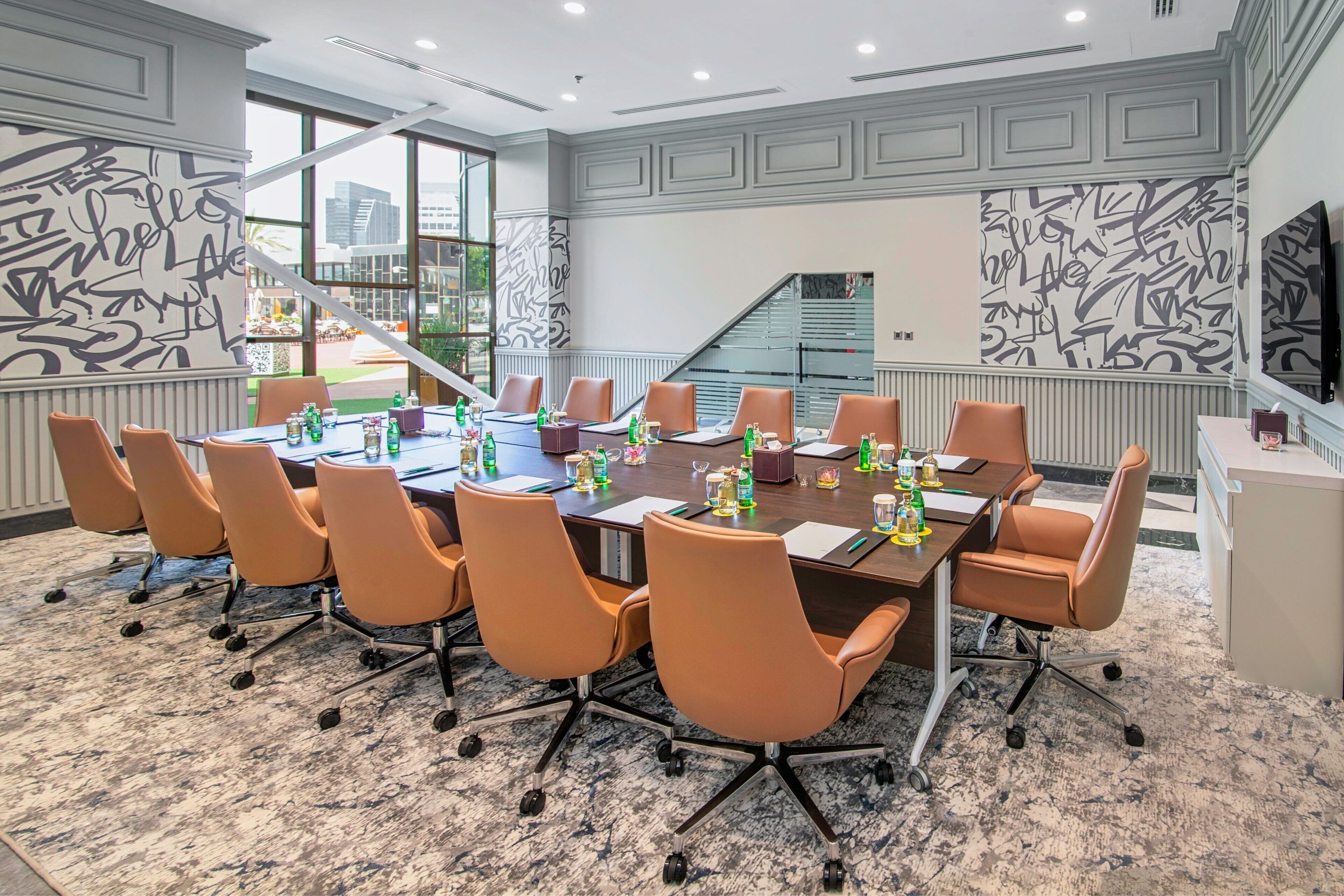 A conference room with a large table, multiple chairs, and a view of a building through large windows.