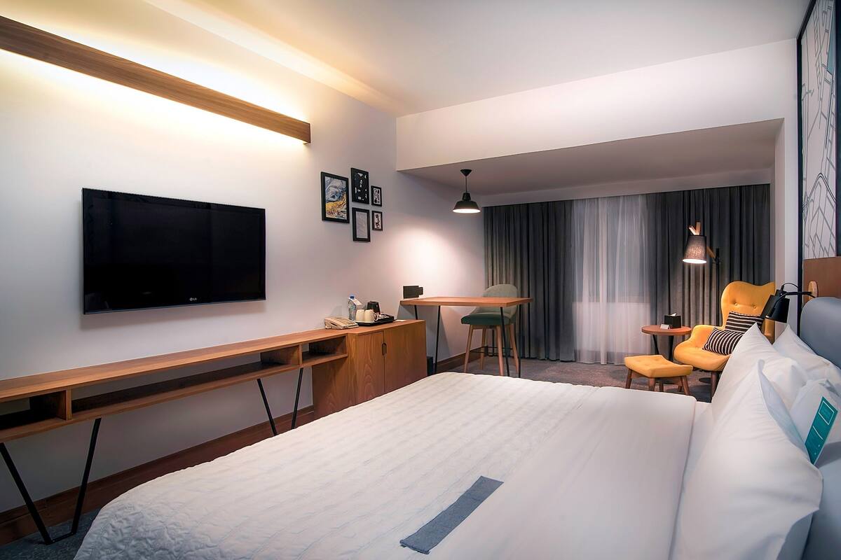 A hotel room with a bed, a desk, a chair, a TV, and a window with curtains.