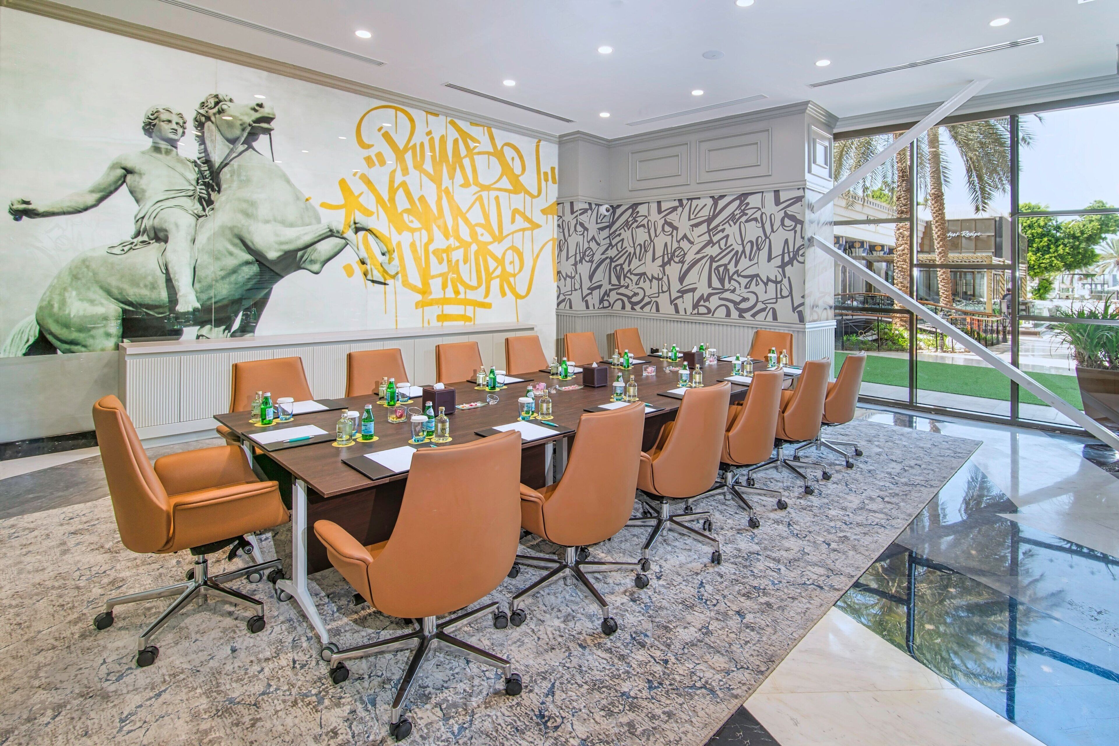 A conference room with a long table, multiple chairs, and a large mural on the wall.