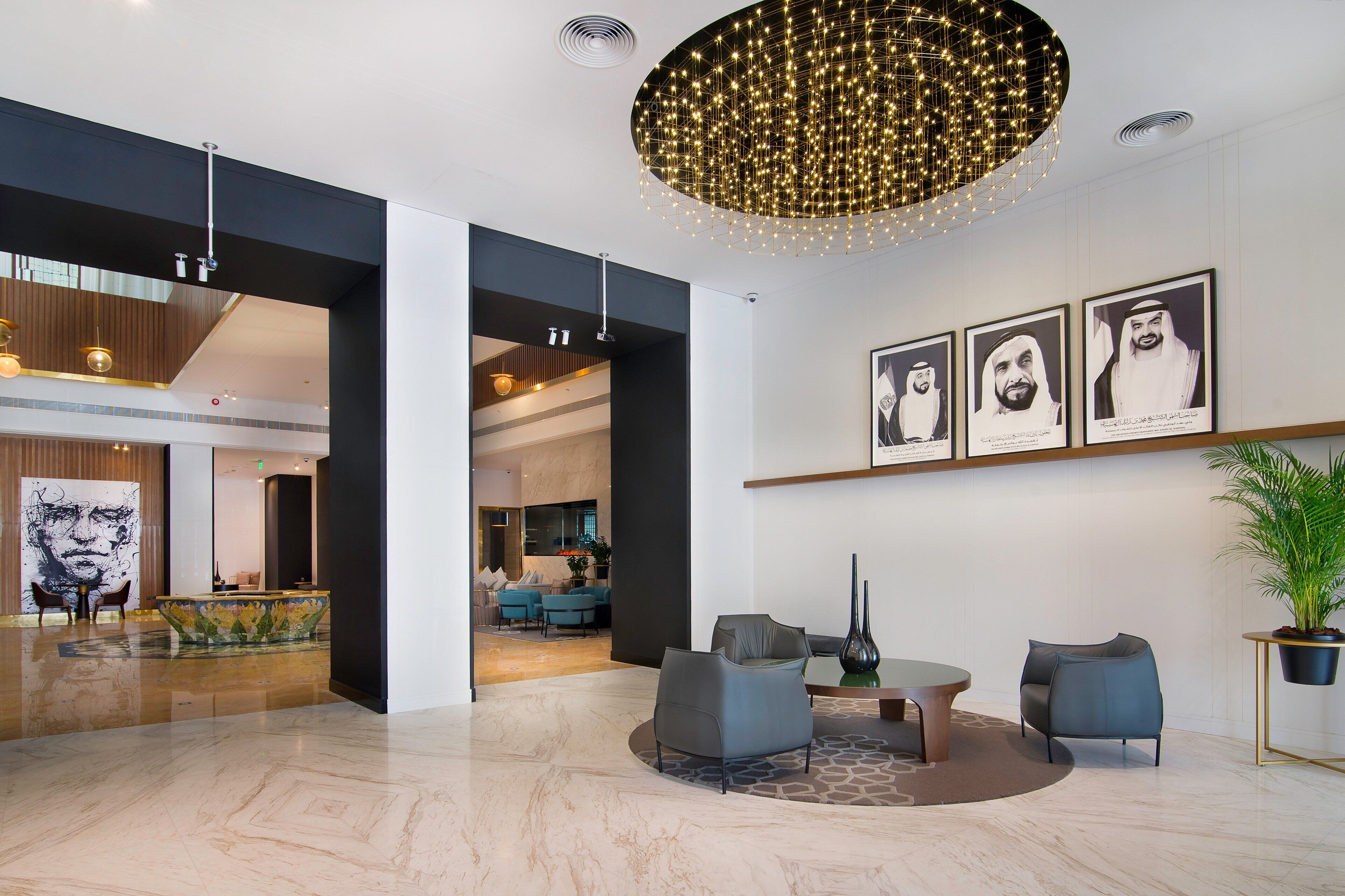 A modern lobby with a marble floor, a round table with chairs, a large abstract painting, and a ceiling light fixture.