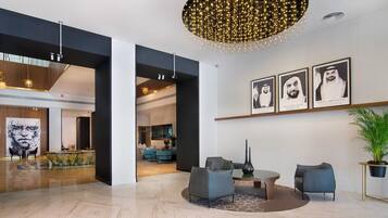 A modern lobby with a marble floor, a round table with chairs, a large abstract painting, and a ceiling light fixture.