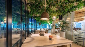 A modern restaurant with a long table, hanging lights, and a view of the cityscape through large windows. - Le Méridien Abu Dhabi Resort (Abu Dhabi)