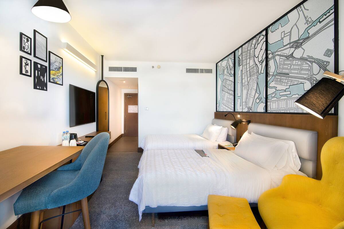 A hotel room with a bed, two chairs, a desk, a TV, and a map on the wall.