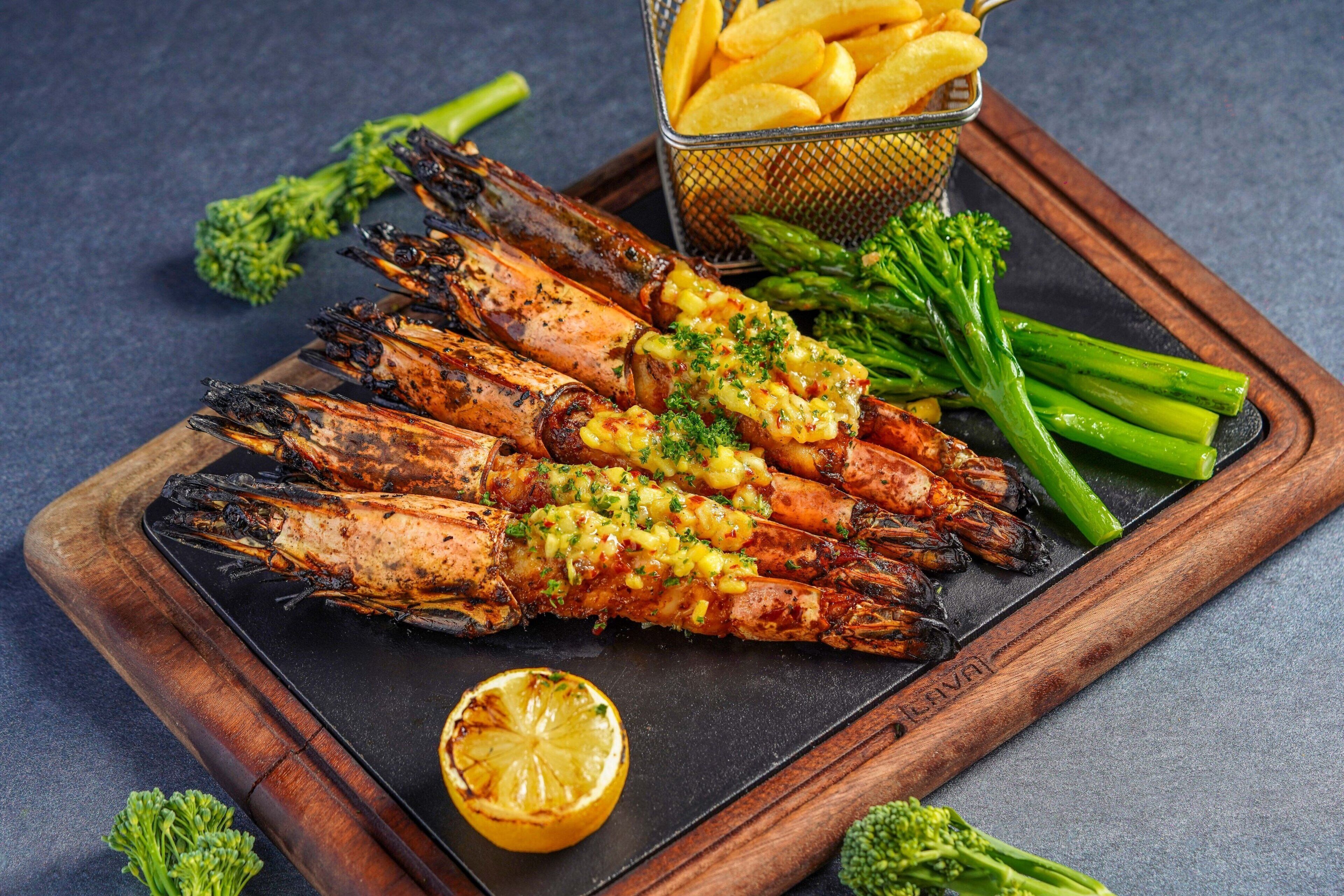 Grilled prawns with a lemon wedge and asparagus on a wooden board.