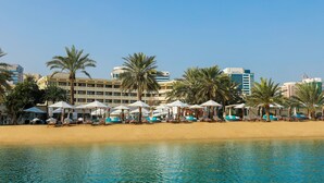 A beachfront hotel with sun loungers and umbrellas, palm trees, and a clear blue sky. - Le Méridien Abu Dhabi Resort (Abu Dhabi)