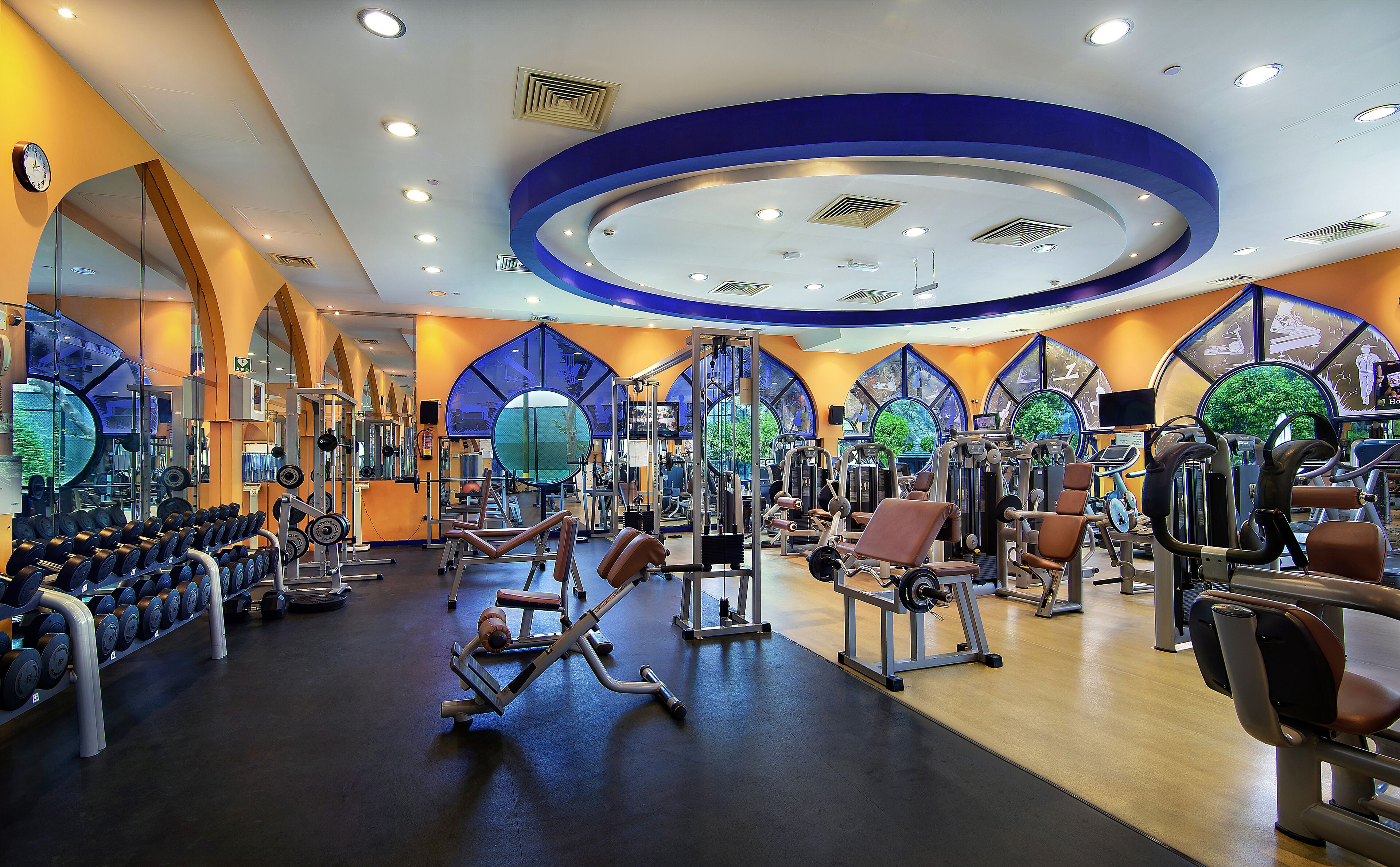 Un gimnasio con diversos equipos de ejercicio, espejos y un diseño de techo circular.