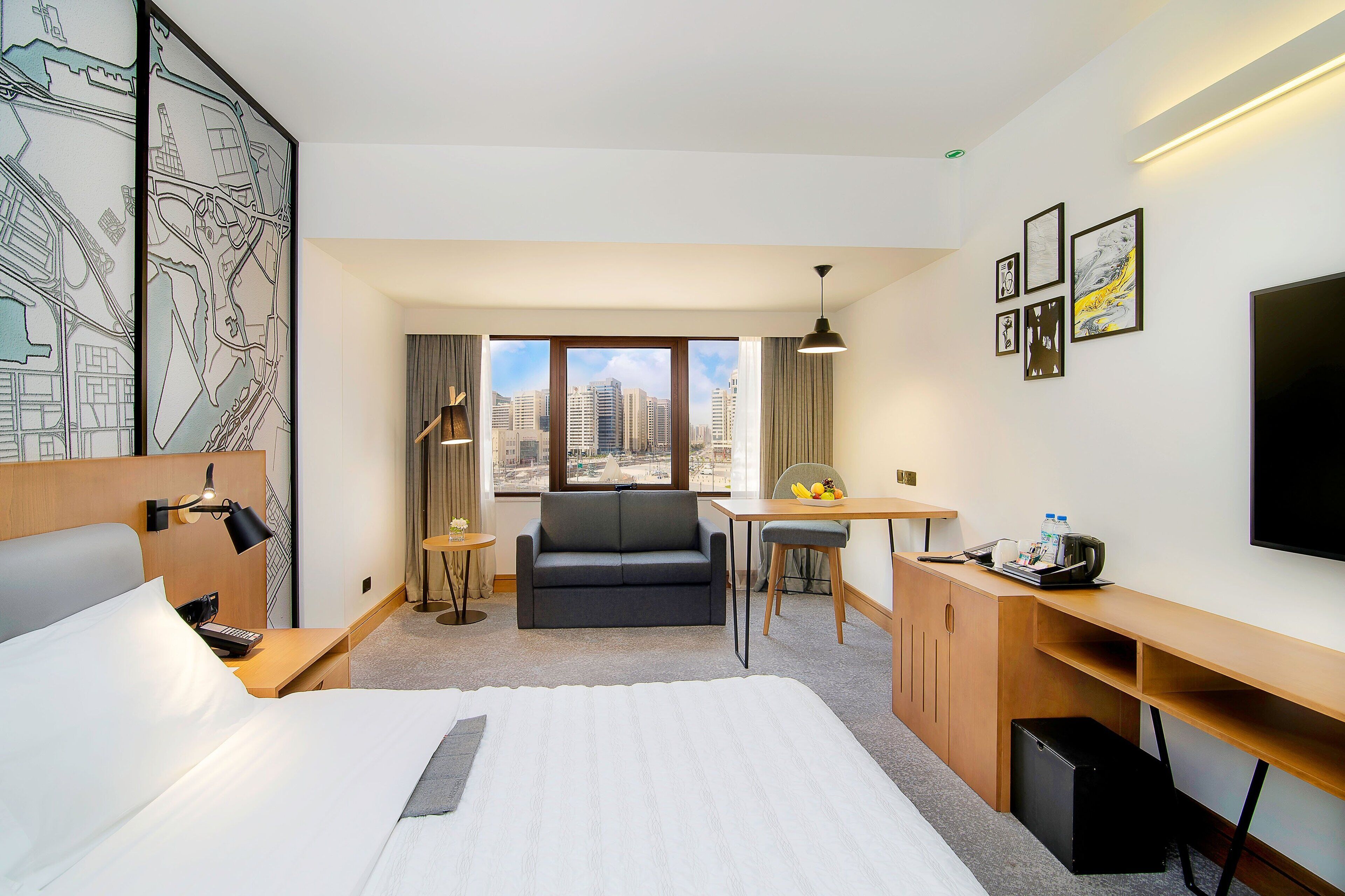 Habitación de hotel con cama, escritorio, sofá, televisor y vista a la ciudad.