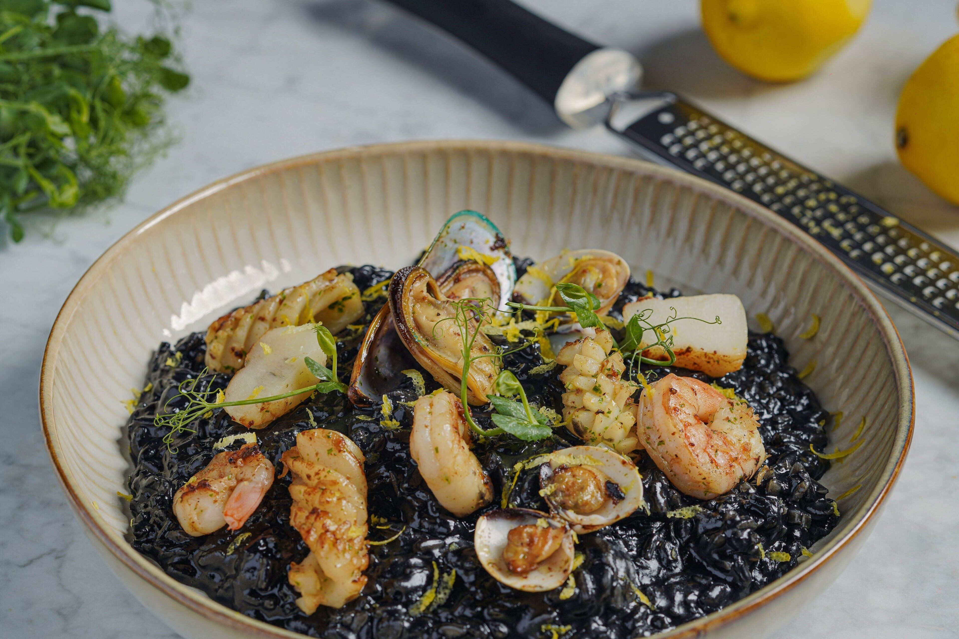 A bowl of seafood risotto with clams and shrimp, garnished with herbs.