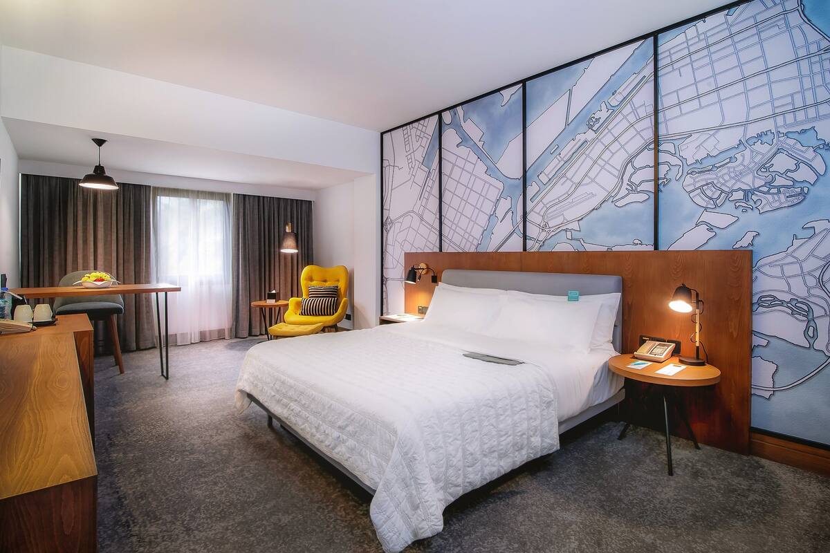 A hotel room with a large bed, a desk, a chair, and a map mural on the wall.