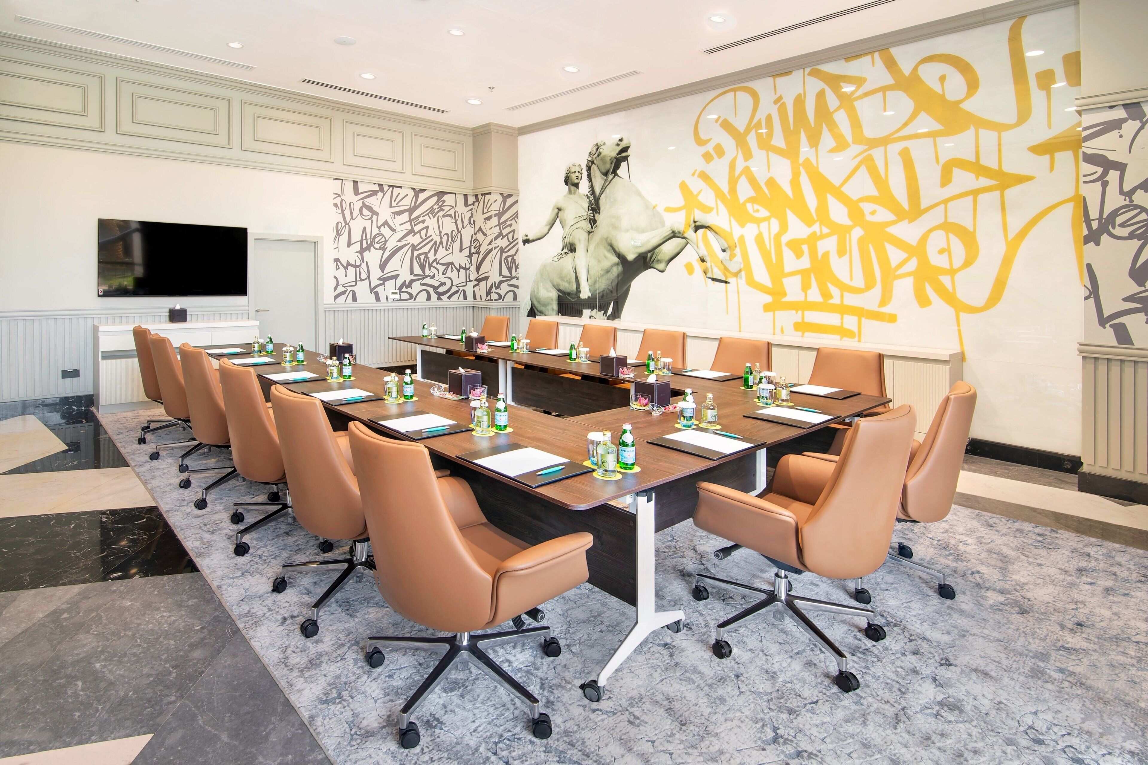 A conference room with a long table, multiple chairs, and a large mural on the wall.
