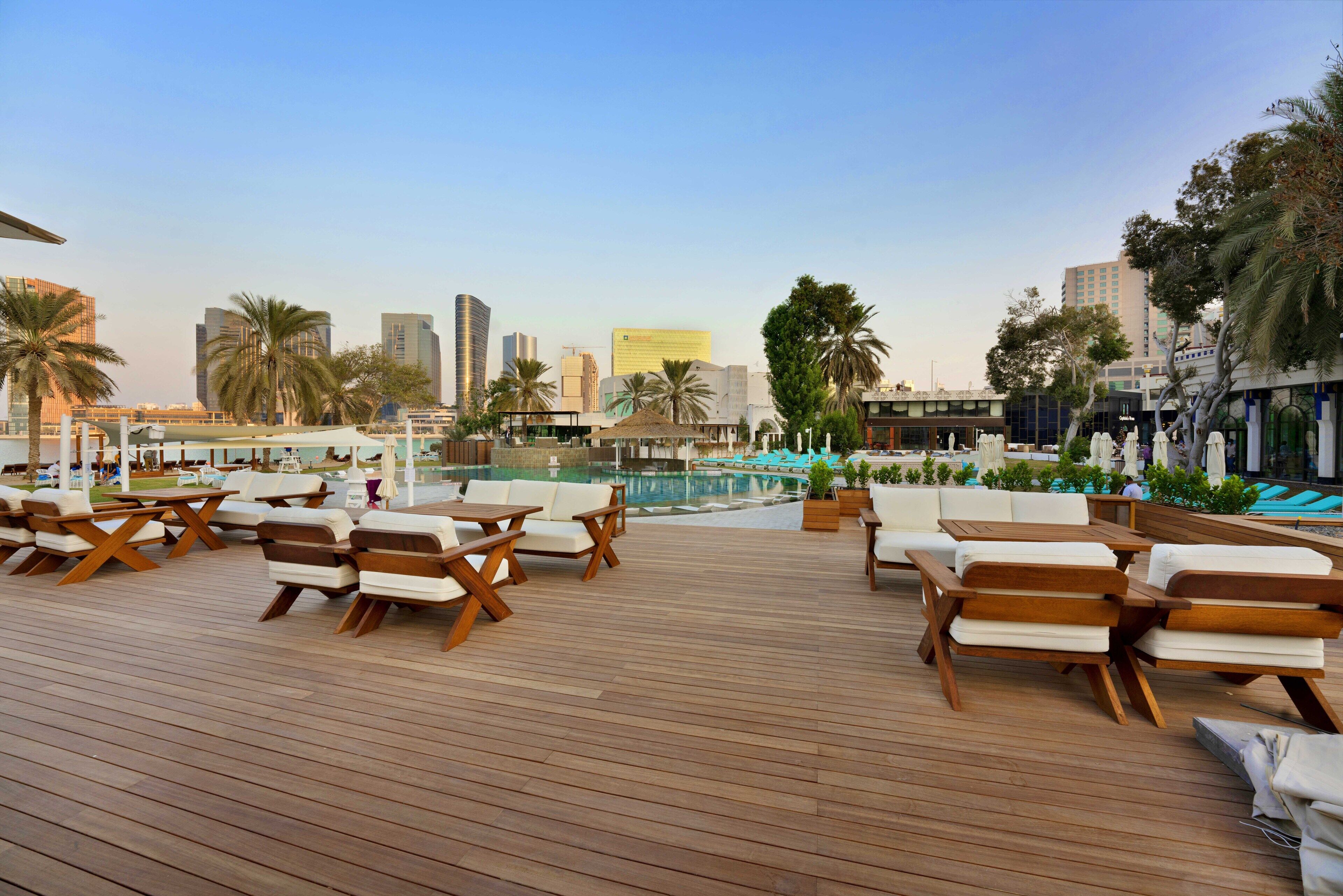 Eine Dachterrasse mit Holzdeck-Sitzgelegenheiten und einem Pool im Hintergrund.