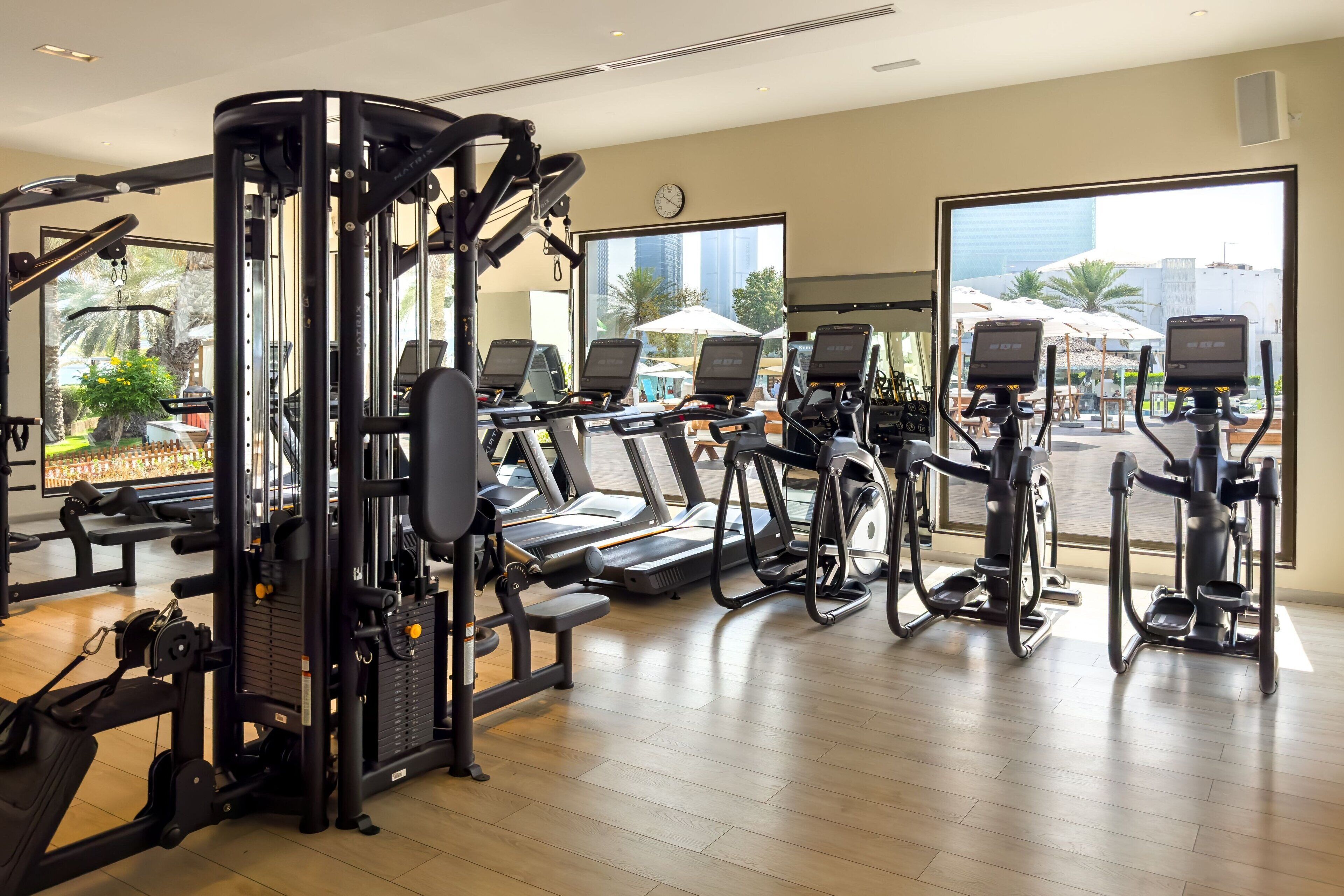 A gym with various exercise equipment, large windows, and a view of the outdoors.