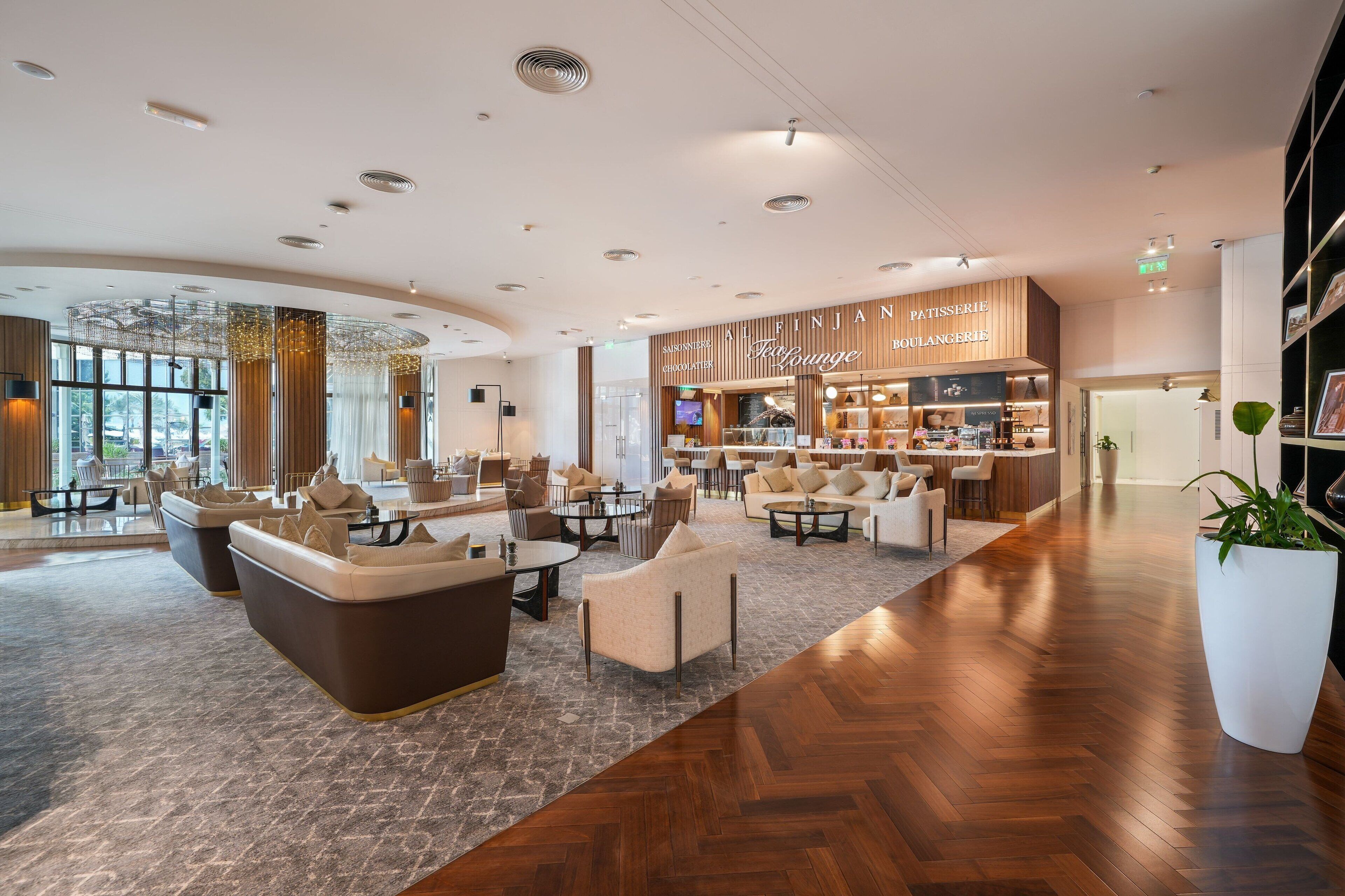 Un hall d’hôtel moderne avec un espace salon, une boulangerie et une grande plante en pot.