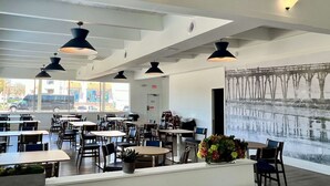 Restaurante moderno com pé-direito alto, iluminação pendente e grandes janelas com vista para a rua.