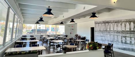 Un restaurant moderne avec de hauts plafonds, des luminaires suspendus et de grandes fenêtres donnant sur la rue.