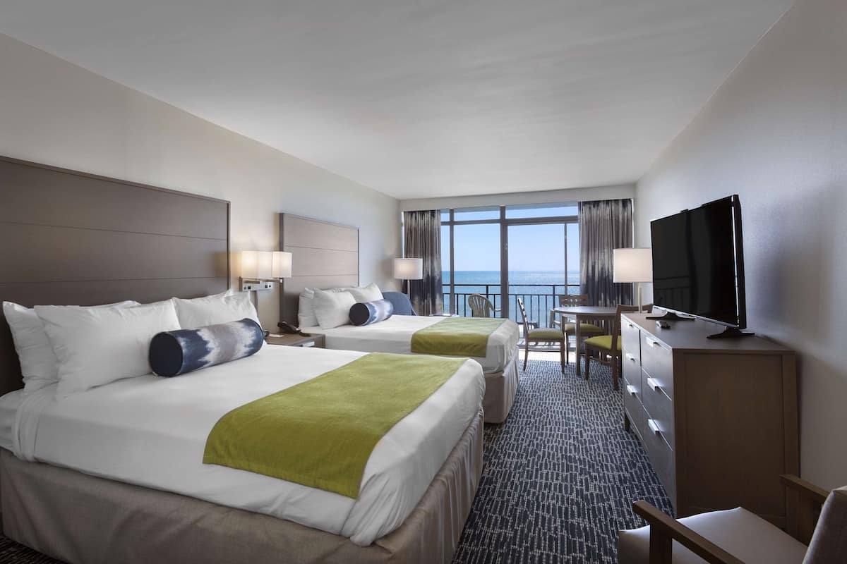Une chambre d’hôtel avec deux lits, un bureau, une télévision et un balcon donnant sur la mer.